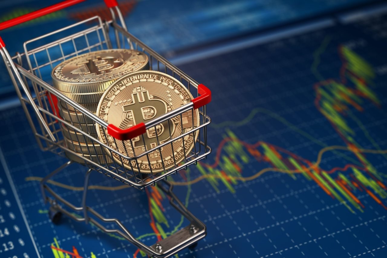 Gold bitcoin coins in a shopping cart on top of a financial trading chart